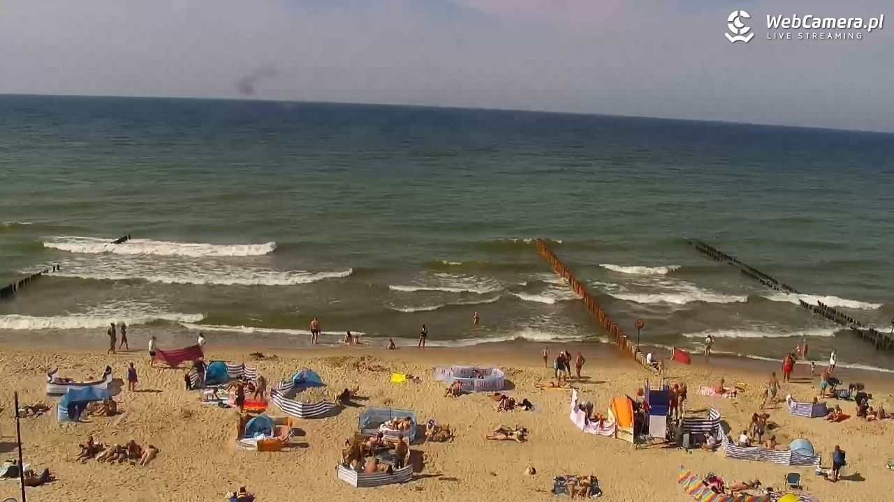 Widok na zatłoczoną plażę w Mielnie i czerwoną flagę na stanowisku ratowników.
