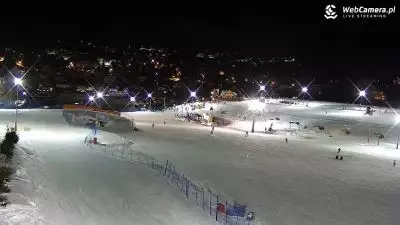 Nocny widok na trasę narciarską, narciarze i snowboardziści zjeżdząjący podczas nocnej jazdy na stacji narciarskiej