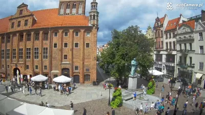 Urlopowicze spacerują starówką w Toruniu i podziwiają pomnik Mikołaja Kopernika Turyści zwiedzający Toruń podczas wakacyjnych wycieczek